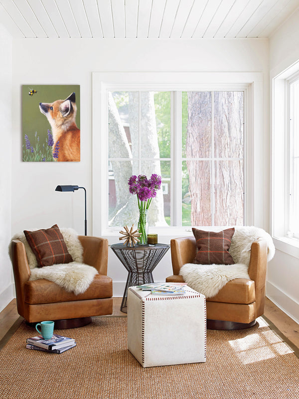 A canvas print depicting a baby fox in profile, looking upwards at a bumblebee in a field of lavender by wildlife artist James Corwin. Hanging in living room wall art home decor.