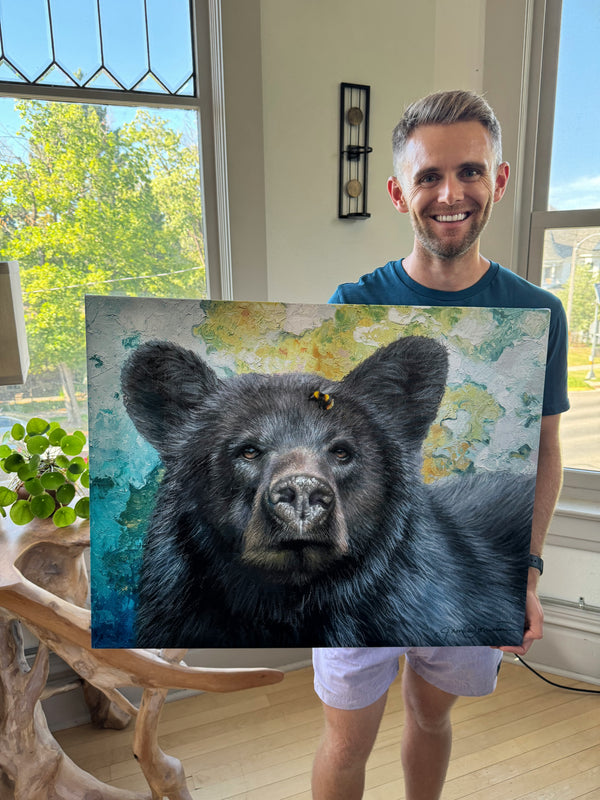 Bumblebee Bear by wildlife artist James Corwin. A Painting of a black bear with a colorful textured background. Artist holding giclee print of the wall art.