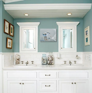 A canvas print of a curious Piping Plover chick standing on a seashore with ocean waves in the background by wildlife artist James Corwin. Hanging in bathroom wall art home decor.