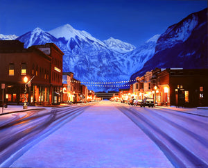 A canvas print depicting a snowy Main Street in Telluride, Colorado, with illuminated lights and snow-covered mountains in the background. Cityscape art by wildlife artist James Corwin.